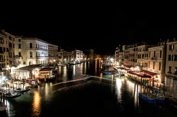 Fototapeta na wymiar A late night long exposure view of the popular Grand Canal in Venice, taken from the top of the Ponte Rialto Bridge, with a light trail set provided by a boat manoeuvring in the moorings.