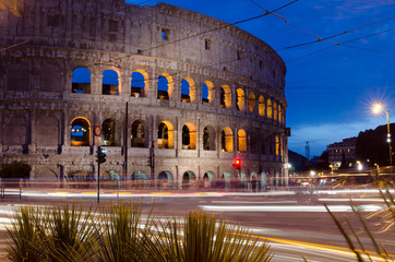 The Colosseum in Rome, Italy at night with traffic streaking past.
