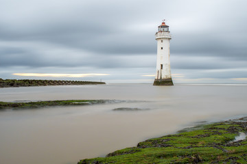 A small inlet in the rocks as the tide comes in by New Brighton Lighthouse, with a small sunset showing in the sky behind.