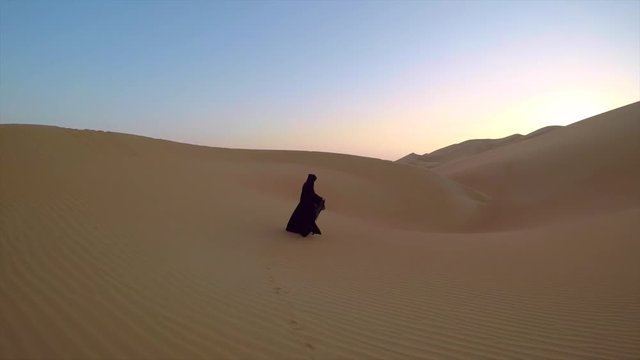 woman in traditional emirati dress, called Abaya, walking in the sand dunes of Liwa desert