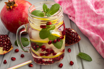 Detox water with pomegranate, lemon and mint on the grey wooden background