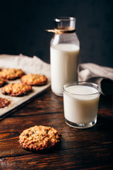 Oatmeal Cookies with Raisins and Glass of Milk for Breakfast. Some Cookies on Parchment Paper with Bottle on Backdrop. Vertical Orientation.