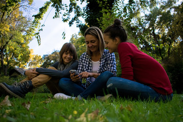 Fototapeta premium Happy family relaxing in grass at the park and using cell phone.