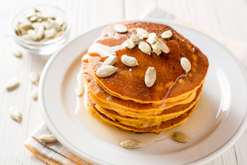 Pumpkin pancakes with honey and pumpkin seeds in plate on white wooden background.