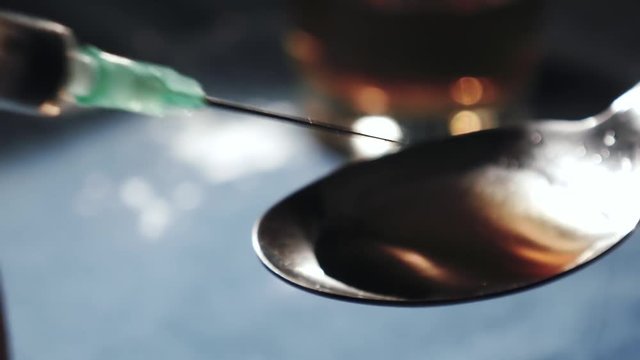 Filling syringe with heroin from a spoon, extreme close up
