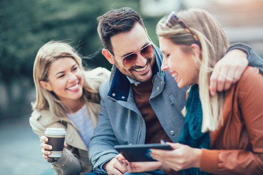Group of smiling friends using digital tablet outdoors