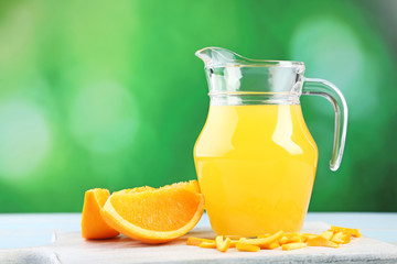 Glass jug with orange juice on wooden table