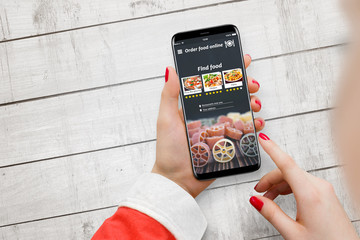 Female Santa Claus ordering food with smartphone app at the white wooden background