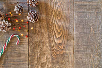 Rustic wood plank background with white tipped pine cones, berries and holiday candy cane on top left corner