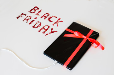 Tablet connected to power black wrapped gift box with a red cord and a Black Friday text written with decorative red little stars