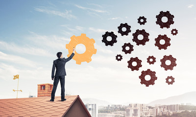 Businessman standing with back on house brick roof and drawing. 