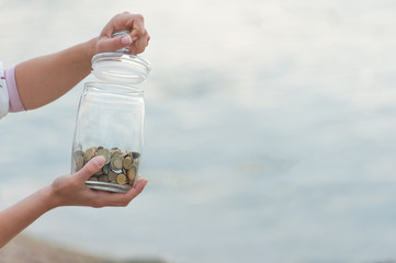 Investment, retirement, taxes and passive income concept. Coins in a glass jar in hand, blur focus