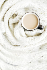 Obraz na płótnie Canvas Coffee mug with milk on white wool scarf. Flat lay, top view.