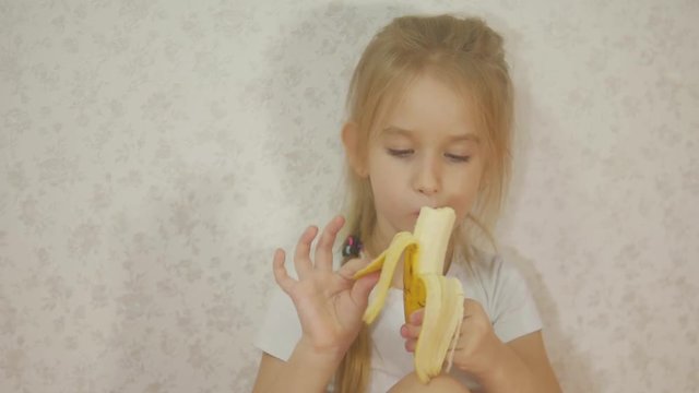Young girl eating banana sitting at home.