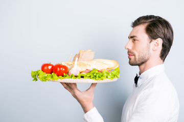 Side view portrait of confident and concentrated young but experienced waiter clothed in white clean uniform with black bow tie. He is carrying an order for the customer, isolated on grey background