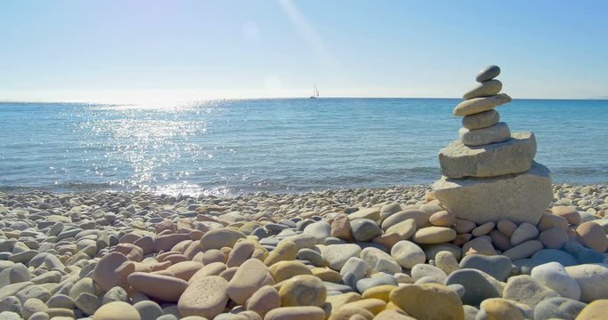 Waves landing on stone beach. Meditation, stone pyramide. Clear blue water.