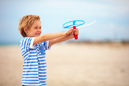 delighted cute young boy, kid having fun on sandy beach, playing leisure activity games with propeller toy