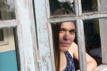 Young woman with long hair looks out of the veranda windows.