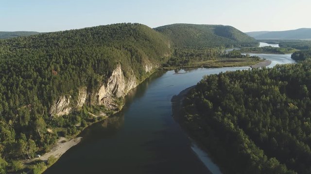 Aerial view of steep bank of river covered with dense virgin forest. Beautiful panorama of summer landscape with bends of water and hills with greenery.