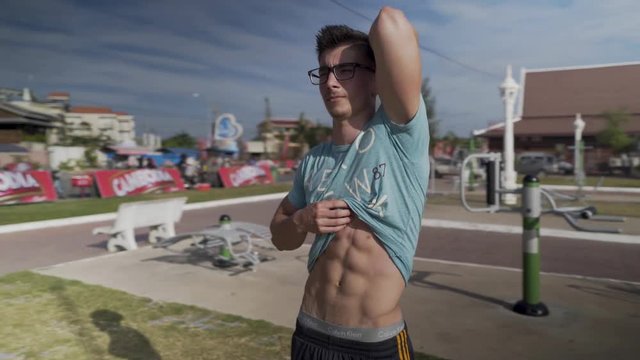 Teenage boy showing off his six pack abdominals and large triceps while lifting his shirt up.