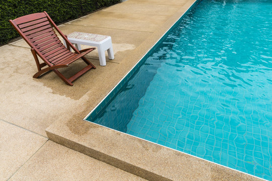 -Wooden Sun Loungers With White Cement Table With Porcelain Tile On Wet Yellow Polished Stone Floor At The Edge Of The Pool