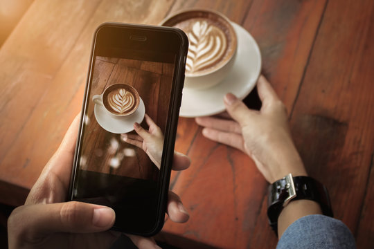 Young girl using Photography of smartphone of latte art coffee o