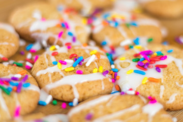 Freshly baked sugar cookies with white icing and rainbow colored sprinkles on wooden board, selective focus