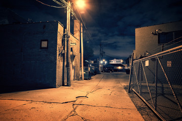 Scary dark city Chicago alley next to an urban warehouse and parking lot.