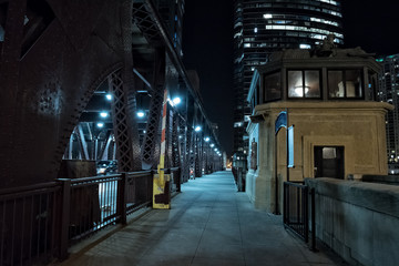 Chicago city vintage river drawbridge with tender house and urban downtown buildings at night.