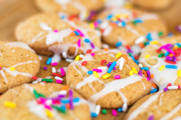 Freshly baked sugar cookies with white icing and rainbow colored sprinkles on wooden board, selective focus