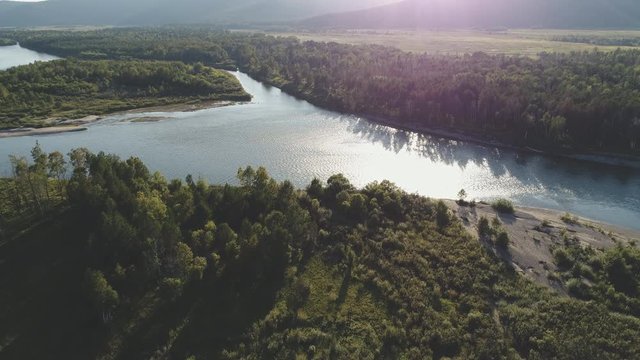 Aerial view of mouth of large river among dense forests at sunset in summer. Green valley covered with green vegetation among junction of huge water area.