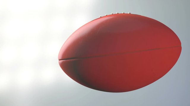 A dirty orange aussie rules ball spinning in slow motion flying through the air on a floodlit stadium background at night