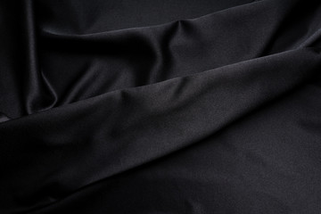 Fototapeta premium Dark black silky, satin fabric, wave, draperies. Beautiful textile backdrop. Close-up. Top view 