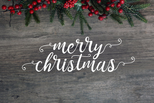Merry Christmas Calligraphy with Evergreen Branches and Berries Over Dark Rustic Wood Background