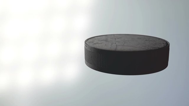 An ice hockey puck caught spinning in slow motion flying through the air scattering water particles in its wake