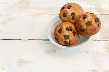 a bowl of chocolate chunk muffins on a rustic white background