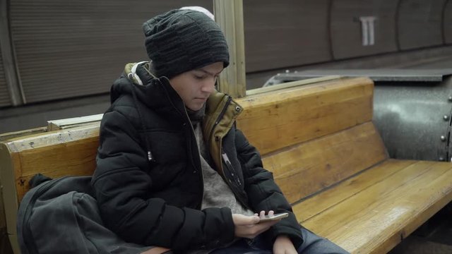 A 15 Year Old Boy In Winter Clothes Is Sitting On A Bench In The Subway.