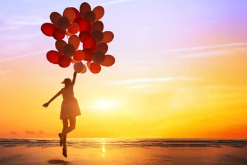 Tuinposter happiness or dream concept, silhouette of happy woman jumping with multicolored balloons at sunset on the beach © Song_about_summer