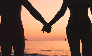 romantic travel, couple on the beach, silhouette of man and woman holding hands at sunset