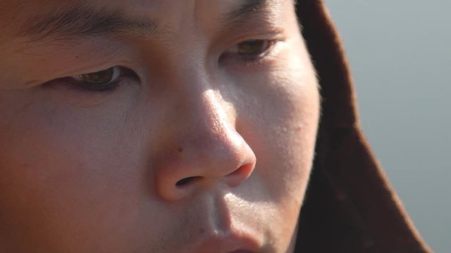 Mongolian archer stands and looks forward in open space. Young man dressed in traditional clothes and helmet looks around his native expanse, thinking about upcoming goals and plans. Experienced