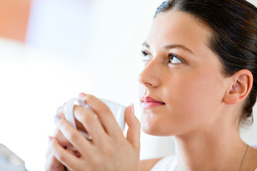Happy young woman with cup of tea or coffee at home
