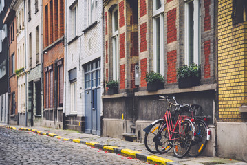 Fototapeta na wymiar January, 1th, 2015 - Ghent, East Flanders, Belgium. Empty street, brick medieval houses facades and parked bike pair. Red bicycle standing near the wall in belgian city Gent.