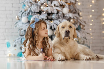 Little cute girl with a golden retriever dog writes letter to Santa near christmas tree