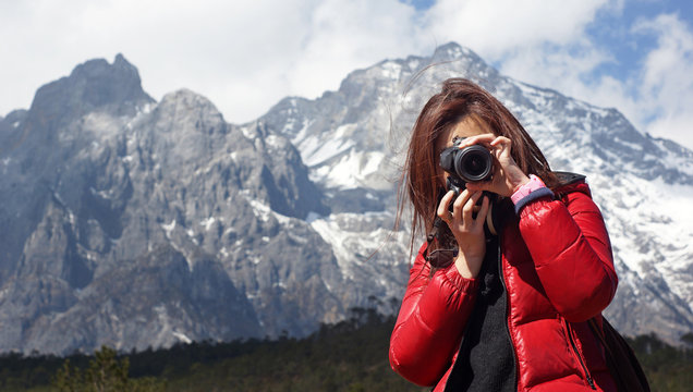 Young girl photographer holding nikon DSLR, she force on other, with snow mountain Jade Dragon background in Lijiang,  in winter, in Yunnan China wide mountain range