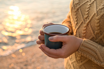 Cozy autumn by the sea. Female hands holding a mug with tea