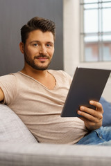 mann sitzt auf dem sofa und hält sein tablet in der hand