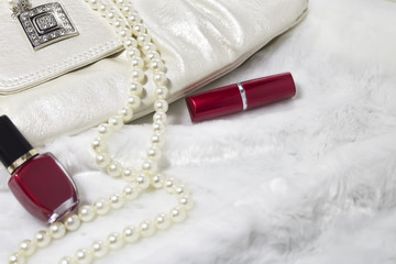 Background. Handbag, nail varnish, lipstick, necklace on white fur rug