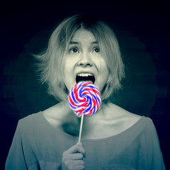 Silly blonde girl teenager licking candy on a stick on a black background. Toned