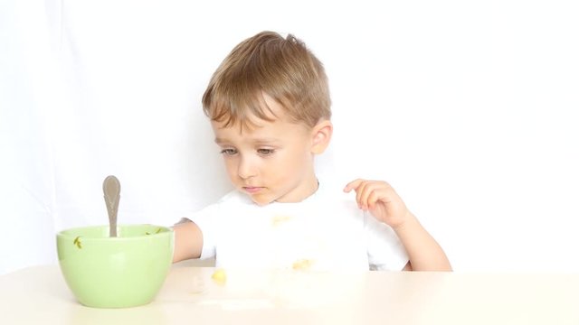 The child boy sitting at the table finished eating food and pushed his plate away