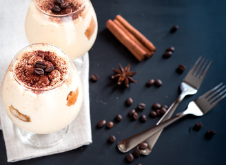 tiramisu in a glass decorated with coffee beans on a dark background, concept of a sweet and luxurious life